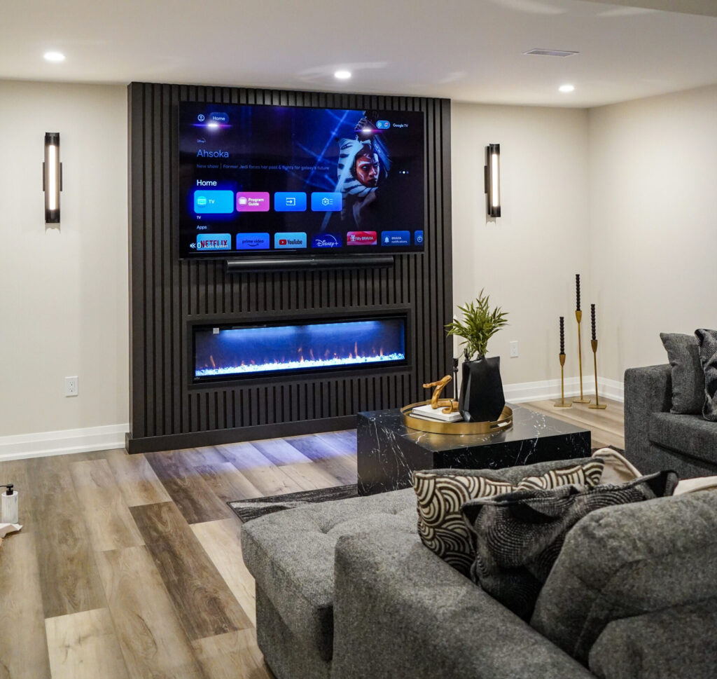 Finished basement with a dark slatted feature wall, a wall-mounted television above a linear electric fireplace, and a sectional sofa.